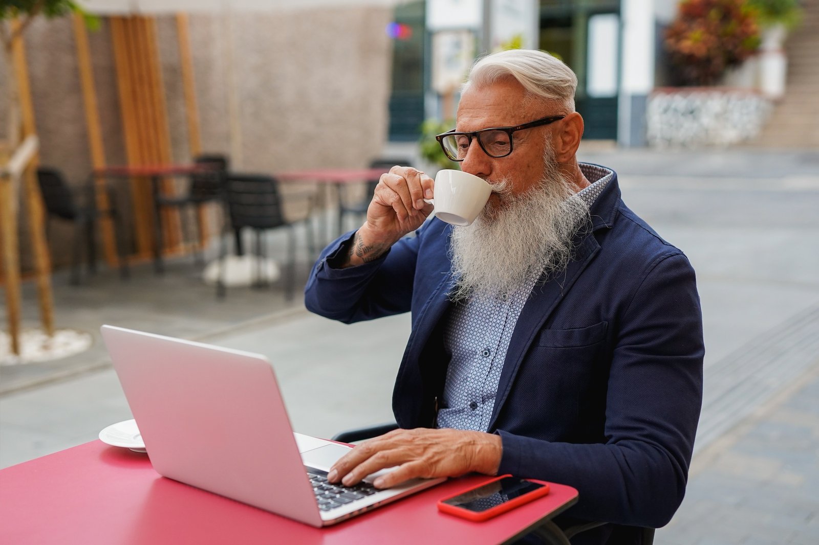 Senior business man using computer laptop while drinking coffee at bar terrace during spring season